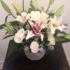 Compact arrangement of cream roses and pink lilies in a gray textured vase on a dark wooden table