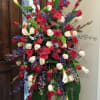 Tall standing spray of red and white roses with purple flowers and white calla lilies on a metal easel.