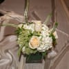 Small wedding centerpiece of ivory roses and white hydrangeas in a glass cube vase