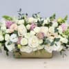 Low centerpiece of white and blush roses with green snapdragons in a gold rectangular vase