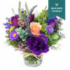 Mixed bouquet of purple and peach flowers in a clear glass vase tied with raffia