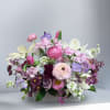 Mixed pink, purple, and white floral arrangement in a low white container