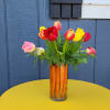 Bright tulip bouquet in a glass vase filled with upright carrots on a yellow table