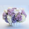 Lavender roses and white orchids arranged in a white vase