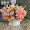 Mixed pink, peach, and yellow roses arranged in a white vase