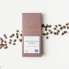 Dark chocolate espresso bar in mauve wrapper with coffee beans scattered on a white surface