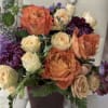 Arrangement of orange and cream roses with purple mums in a dark square vase