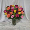 Tall clear vase filled with mixed red, pink, orange, and yellow roses with small yellow filler flowers