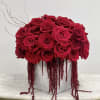 Compact arrangement of red roses with trailing red accents in a gray cube vase on a small table