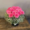 Round arrangement of bright pink roses with a collar of white filler flowers in a black hatbox.