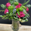 Vase arrangement of hot pink roses, green mums, and hydrangea with looped variegated leaves in a clear glass vase