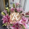 Pink lilies and roses arranged around a white floral letter R.