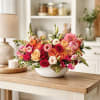Mixed bouquet of pink, orange, and white flowers in a white bowl vase