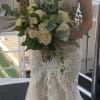Bride holding a hand-tied bouquet of ivory roses with abundant greenery