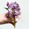 Small handheld boutonniere of purple and pink flowers with a gold ribbon-wrapped stem.