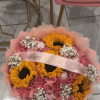 This flower arrangement features tightly packed sunflowers, pale pink roses, ruffled pink