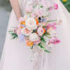Bride holding a pastel bouquet of pink, white, and orange flowers