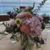 Pastel floral centerpiece in a low square vase on a table by the water