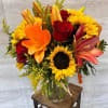 A warm, autumn-inspired arrangement featuring sunflowers, red roses, orange lilies, and golden