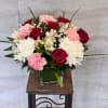 Bouquet of red roses, pink carnations, and white chrysanthemums in a glass vase