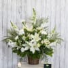 White floral arrangement in a woven basket with a candle beside it
