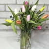 Tall clear vase of mixed pink, white, yellow, and orange tulips with filler flowers