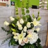 White lilies and roses arranged in a tall vase with green accents