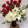 Tall arrangement of red roses, white lilies, and white hydrangeas in a red glass vase