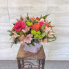 Mixed pink and orange flowers arranged in a square glass vase