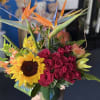 Tropical arrangement with birds of paradise, red roses, sunflower and lilies in a glass vase