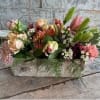 This stunning centerpiece features seasonal blooms in soft peaches and pinks, presented