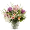 Mixed bouquet of purple roses, peach spray roses and white hydrangeas in a clear glass vase
