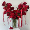 Red roses arranged in a clear ribbed vase with red ribbons