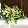 Green and white casket spray with roses, hydrangea, and other flowers on a white casket