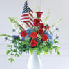 Red roses and blue-white flowers in a white vase with small American flags
