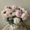 Large bouquet of pale pink and white peonies in a white vase