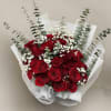 Hand-tied bouquet of red roses with white filler flowers and tall greenery wrapped in white paper.