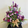Pink and purple mixed flower arrangement with a gold ribbon in a basket