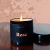 Lit black candle in a round container labeled Rose