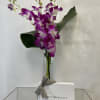 Purple orchids in a glass vase with a white chocolate box tied by a gray ribbon.