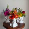 Three colorful flower arrangements in white face-shaped vases on a round table