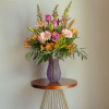 Mixed pink and orange flower arrangement in a purple vase