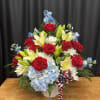 Red roses, yellow lilies, and blue hydrangeas in a white vase