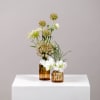 Two small floral arrangements in amber glass vases on a white pedestal