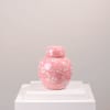 Pink ceramic jar with floral and bird pattern on a white pedestal