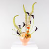 Tall floral arrangement with orange blooms and dark calla lilies in a peach vase