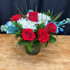 Red roses and white daisies in a glass vase with blue accents