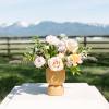 Low arrangement of white and peach roses in a matte yellow pedestal vase set outdoors.