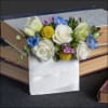 White roses and blue flowers arranged in a white ribbon-wrapped holder
