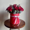 Red roses arranged in a red hat box with a white ribbon